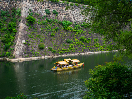 The tourists are having sight seeing moment around the great construction of japanese Osaka castle's. The gold vintage style boat is traveling along the lake surrounding the castle.の写真素材