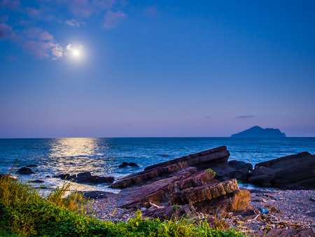 The beauty moment of moon nature and sea. The great supermoon is shining above the Pacific ocean. The moonlight is so strong, the light reflect to the sea in long and wide way toward the rocky shore.の写真素材