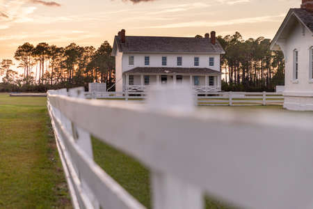 A white wooden fence and a house in a rural setting at sunset.