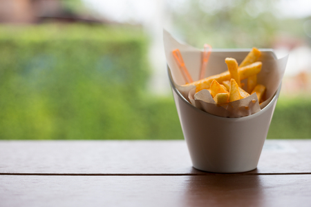 French fries in a white cup on a wooden table.