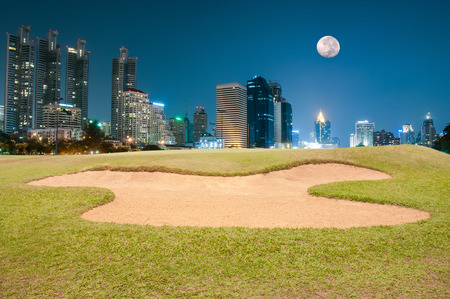 Sand bunker on the golf course with illuminated buildings on the horizonの写真素材