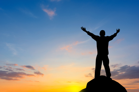 Silhouette of man raised hands at sunsetの写真素材