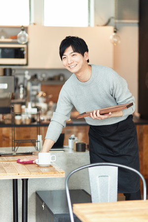 Portrait of a young man standing at the counter of coffee shopの写真素材
