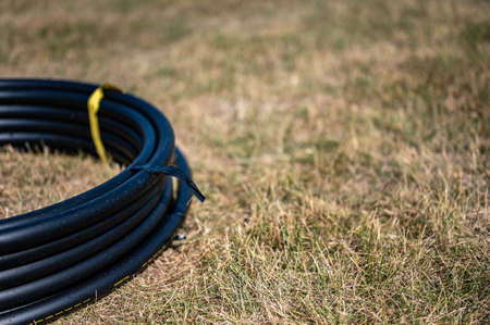 Coil of 1 inch irrigation tubing ready for new installation on top of brown and damaged dry grass.の写真素材