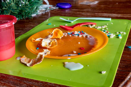 Mess left at the kitchen table after a toddler finished. Plastic fork, cup and plate strewn with...