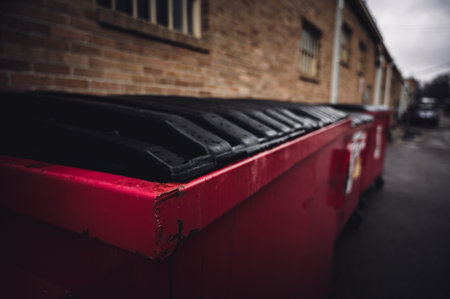 row of covered garbage bins along a brick wall in a back alleyの写真素材