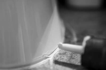 Selective focus on silicone caulking ready to be applied around the seal of a bathroom toilet.の写真素材