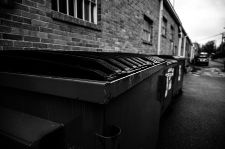 row of covered garbage bins along a brick wall in a back alleyの写真素材