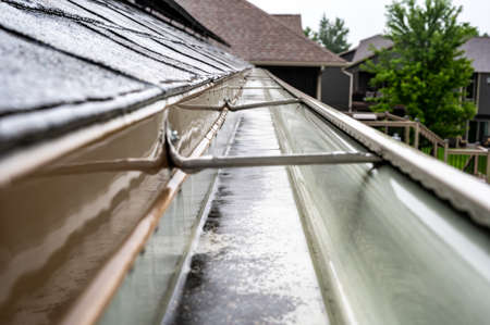 Selective focus on a section of residential guttering with hanger conveying water during a storm. Rain splatters and drops visible.の写真素材