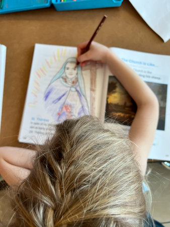 Selective focus of top of young girls head with a blurred biblical drawing being colored below.の写真素材