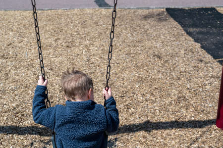 Preschool Caucasian boy on a swing over a woodchip base.
