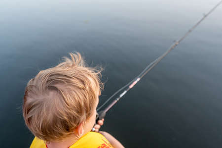 Boy on a fishing with blue water in backgroundの写真素材