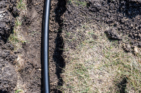Focus on a black 1 inch sprinkler plastic water line laid in a shallow trench