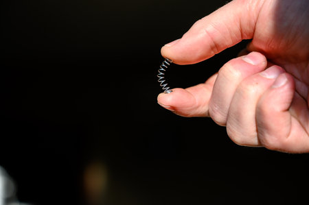 Caucasian hand compressing a metal spring between a thumb and fingerの写真素材