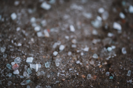 macro ground level closeup view of rock salt ice-melt on concrete with a frozen layer.