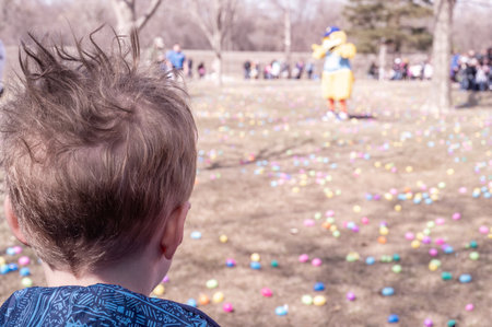 Selective focus on a single child looking out over a field of plastic Easter eggs at a public...