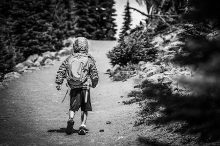 young child wearing a backpack and jacket on a hike up a dusty trail.の写真素材