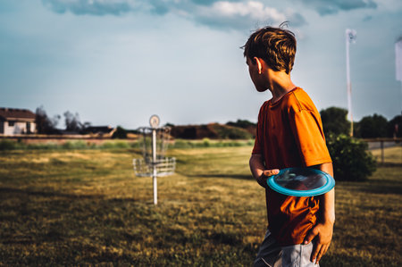 Young Caucasian male boy aiming a disc golf at a chain goal.の写真素材
