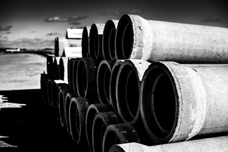 Monochrome photo of stacked concrete pipes against sky