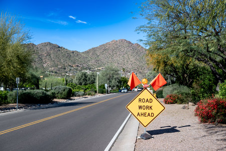 Road Work Ahead sign and flags posted on a road with construction in the background.