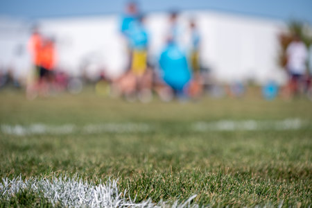 Selective focus on flag football grass with blurred youth team huddle in the background
