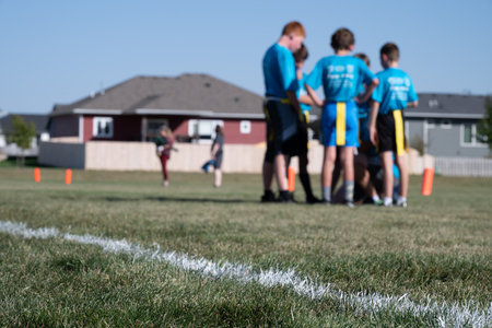 Selective focus on flag football grass with blurred youth team huddle in the background