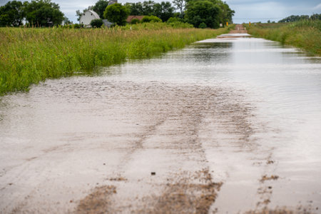 Selective focus on the gravel leading into floodwater covering the road in a rural areaの写真素材