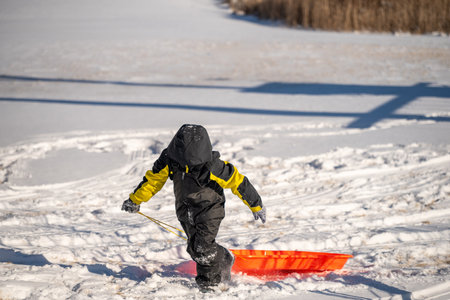 Child pulling a sled up a snow covered hill covered with tracksの写真素材