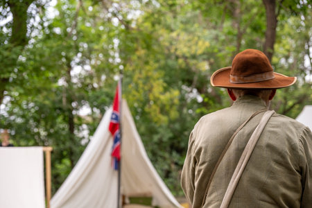 Historical reenactor stands near flag and camp, surrounded by trees during a living history eventの写真素材