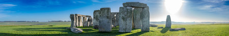 Visitors explore Stonehenge in the early morning light surrounded by green grass and clear skiesの写真素材