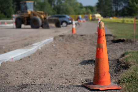 Construction work in progress on a road with equipment and traffic cones during daytime on a sunny...