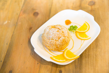 Eclair or profiterole with orange sauce on the white ceramic dish on wooden table, Delicious profiteroles dessertの写真素材