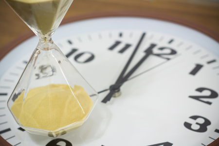 yellow hourglass on wall clock on wooden backgroundの写真素材