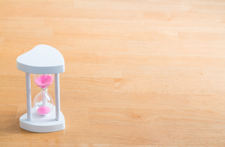 pink hourglass with white wooden frame on light wooden tableの写真素材
