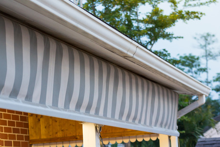 grey and white striped awning under rain gutters of roof in evening lightの写真素材