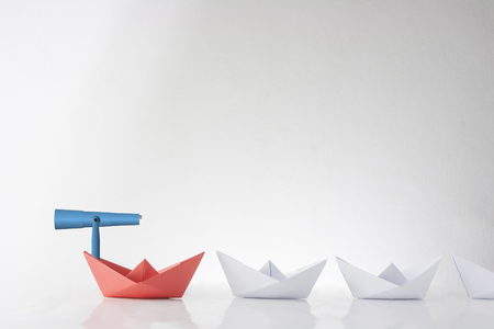 The red paper boat paves the way for white boats. Metaphor of followers and leader. Close-up view.の写真素材