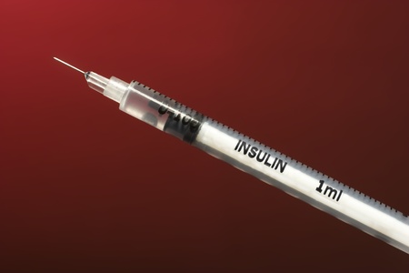 closeup view of small white insulin syringe with medicine on dark red backgroundの写真素材
