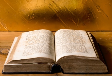 opened antique jewish bible lies on wooden table in front of golden wall