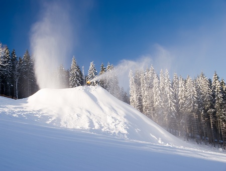 snow guns and makers in action in winter on the snowy hill with forest in backgroundの写真素材