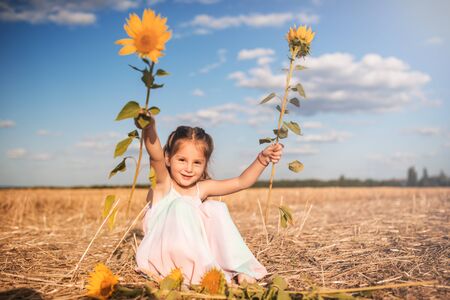 Charming girl in a long sundress sits on a fieldの写真素材