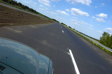 Tilted angle shot a smooth highway surrounded by beautiful summer nature with green grass and blue sky with clouds on a sunny summer hot day. Fast ride conceptの写真素材