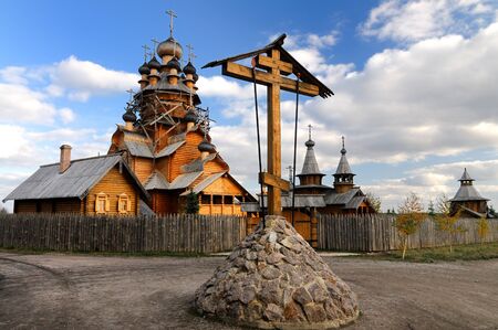 Russian old wooden church and house stands behind a wooden fence on a sunny warm summer day. The...