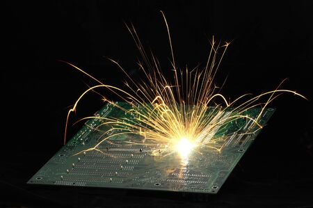Bright burning sparks fly from the chip of complex electronic equipment on the dark background....