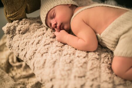 Cute little newborn baby in a knitted suit lies on a soft plaid and smiles in a dream. The concept...