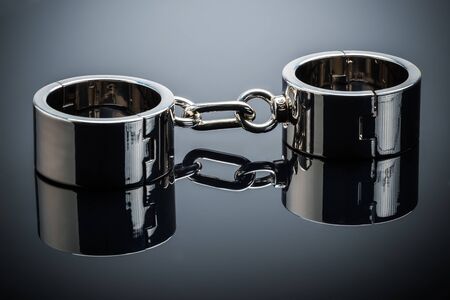 Gold handcuffs lie on a gray metal mirror surfaceの写真素材