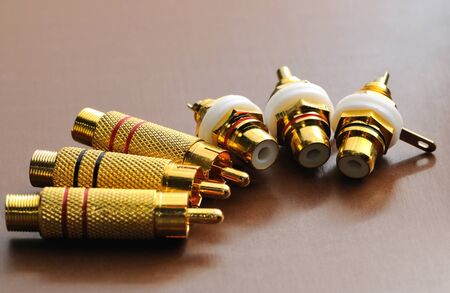 Close-up four golden plugs stand and lie flat on a glossy table in dark lighting. Concept of audio...