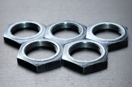 Five chrome metal nuts in the shape of honeycombs lie next to each other on a metal table. The...