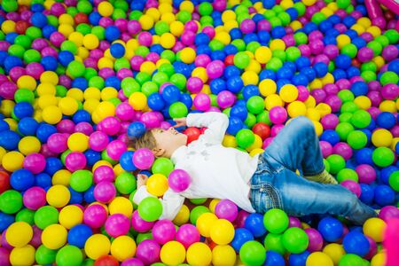 Cute girl in childrens clothes plays in the pool with bright plastic balls of different colorsの写真素材