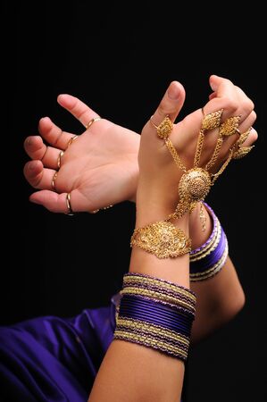 Female hands in massive jewelry as golden bracelet and rings. Movement of national indian dance. Isolated on dark backgroundの写真素材