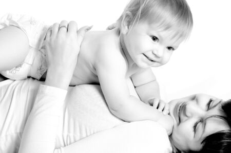 Pretty blond little baby boy lying on mother. Woman holding her son on belly. Family portrait on...